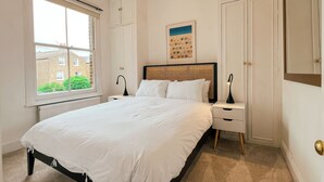 A bedroom with a bed, bedside tables, a window, and a door. - Sugden Road (London)