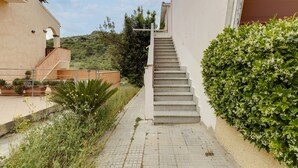 A residential building with a staircase leading to a second floor, surrounded by greenery and a hilly landscape. - Apartment With sea View Terrace and air Conditioning (Castelsardo)