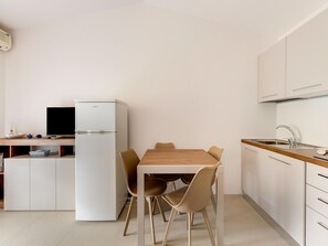 A compact kitchen with a dining table, chairs, a refrigerator, and a sink. - Apartment With sea View Terrace and air Conditioning (Castelsardo)