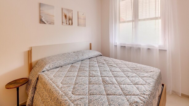 A bedroom with a bed, a bedside table, a window with sheer curtains, and three wall-mounted pictures. - Apartment With sea View Terrace and air Conditioning (Castelsardo)