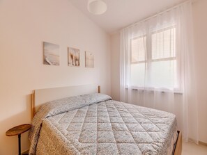 A bedroom with a bed, a bedside table, a window with sheer curtains, and three wall-mounted pictures. - Apartment With sea View Terrace and air Conditioning (Castelsardo)