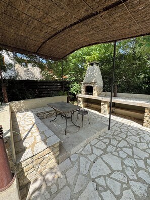Une terrasse extérieure avec une table en pierre, des chaises et un four en pierre.