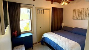 A bedroom with a bed, a desk, a chair, a ceiling fan, and a window.