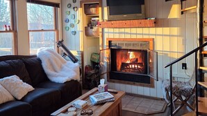 A cozy living room with a fireplace, a sofa, a coffee table, and a TV mounted on the wall.