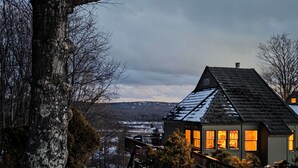 A house with a sloped roof, a visible chimney, and a snow-covered landscape.