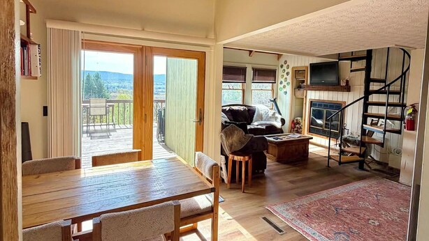 A spacious room with a wooden dining table, a sofa, and a staircase leading to an upper level.