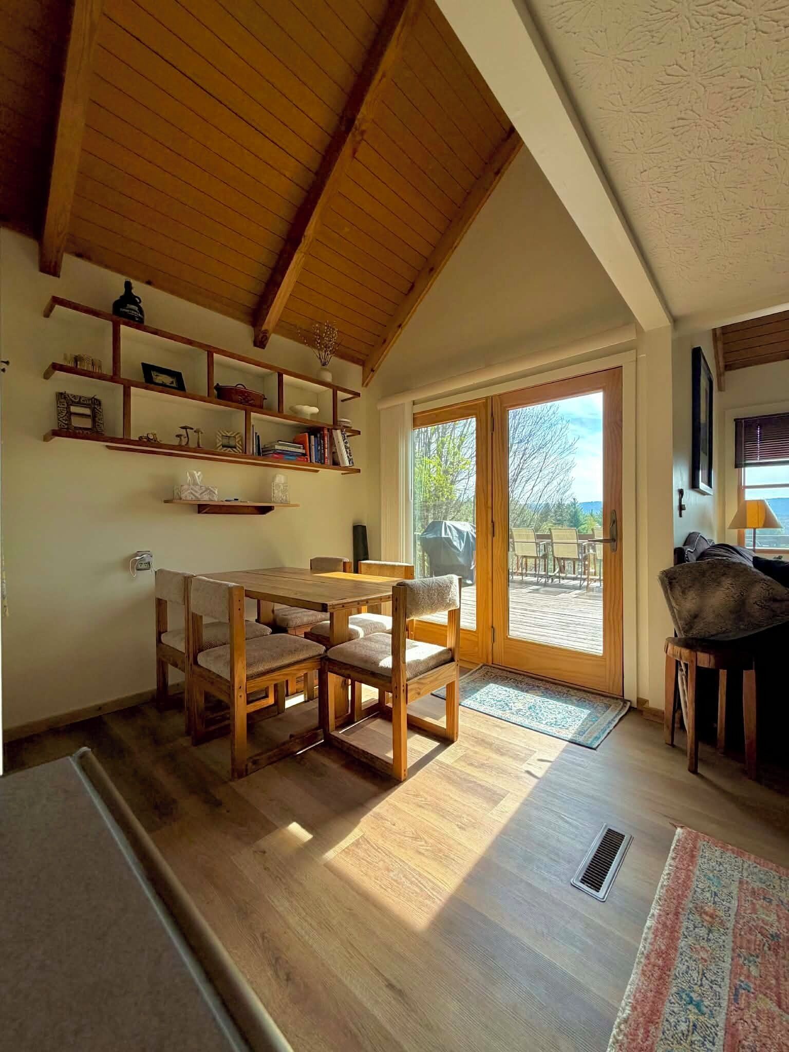 A cozy room with a wooden dining table and chairs, a bookshelf, and a view through a glass door to an outdoor patio.
