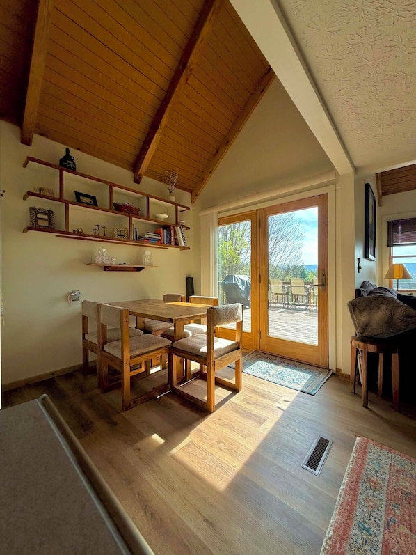 Ein gemütliches Zimmer mit einem Holzespeisetisch und Stühlen, einem Bücherregal und Blick durch eine Glastür auf eine Terrasse.