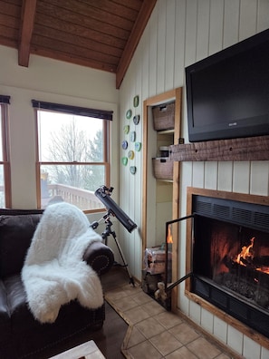Ein gemütliches Wohnzimmer mit Kamin, Wandfernseher und Teleskop.