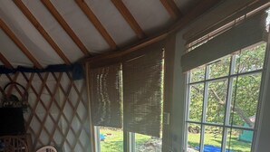 Une pièce avec un plafond en bois, un tapis à motifs, une chaise et une vue sur un jardin avec une table de pique-nique.
