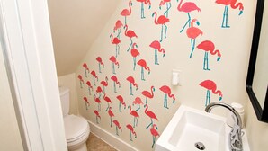 Ett badrum med toalett, handfat och en vägg med ett mönster av röda flamingos.