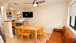 Ett kompakt bostadsutrymme med en matplats, ett litet kök och en soffa placerad vid ett fönster.