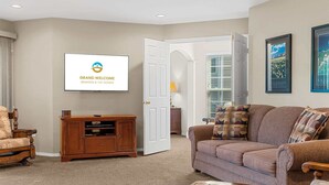 Ein Wohnzimmer mit einem Fernseher, der 'Grand Welcome' und 'Branson & The Ozarks' zeigt, einem Holz-Entertainment-Möbel und einem braunen Sofa, sowie einer Tür zu einem anderen Raum.