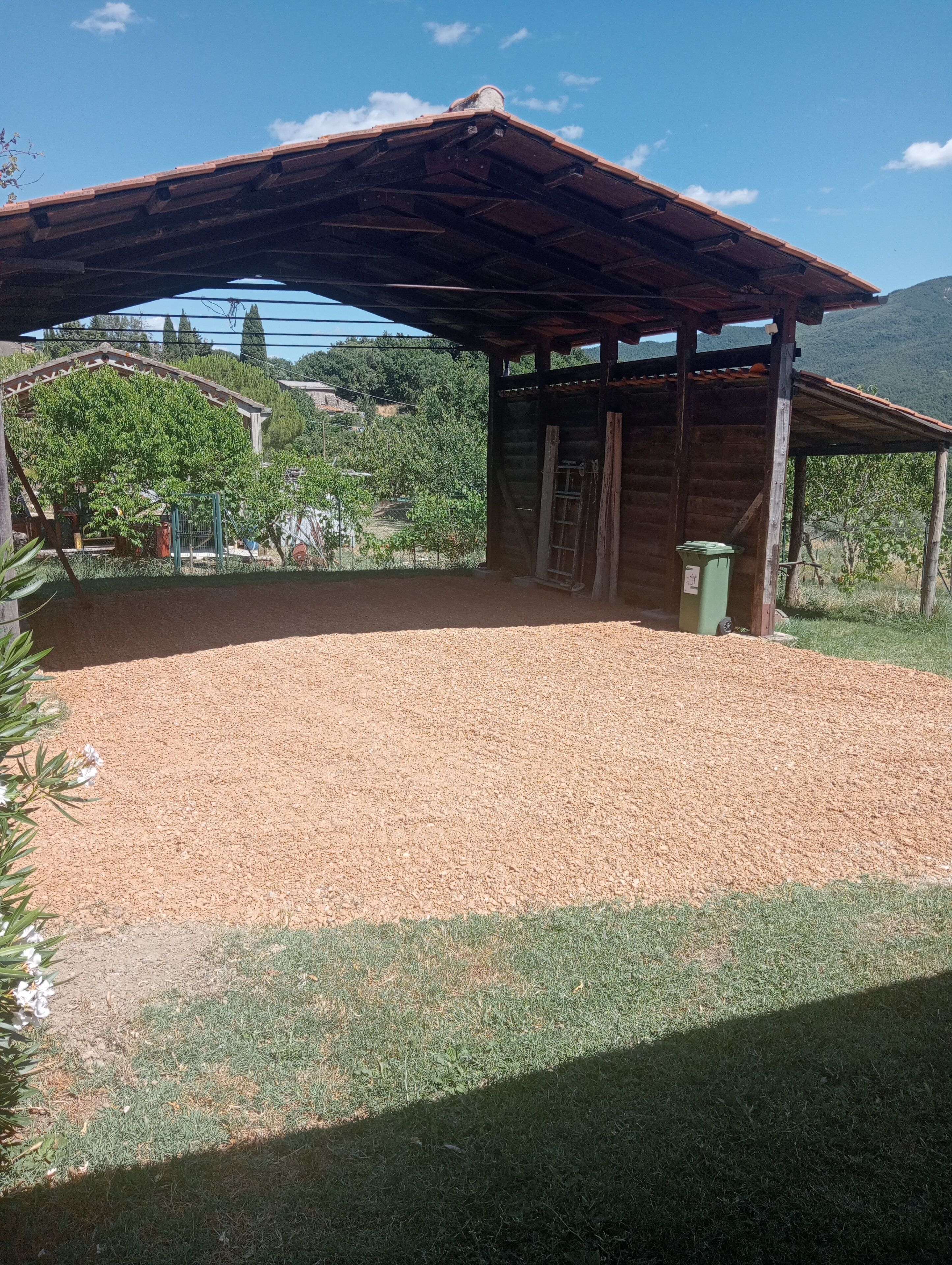 Un espace extérieur abrité, doté d’un sol en gravier, d’une structure en bois et entouré de verdure.
