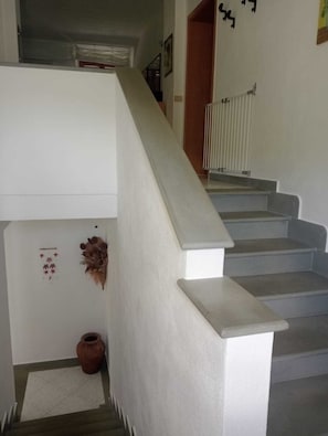 Una escalera con barandilla blanca y peldaños, un pequeño jarrón decorativo y un radiador en la pared.