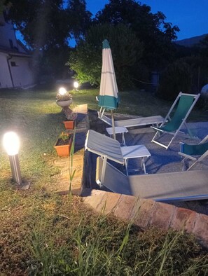 Ein Garten mit einer Terrassenfläche, inklusive Tisch, Stühlen und Sonnenschirm.