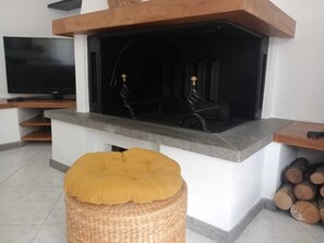 Una sala de estar con chimenea, televisión y un reposapiés de mimbre.