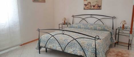 A bedroom with a bed, two bedside tables, a lamp on each table, a patterned bedspread, and a painting on the wall.