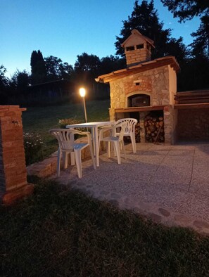 Eine Terrasse im Freien mit einem gemauerten Pizzaofen, einem Tisch und Stühlen.