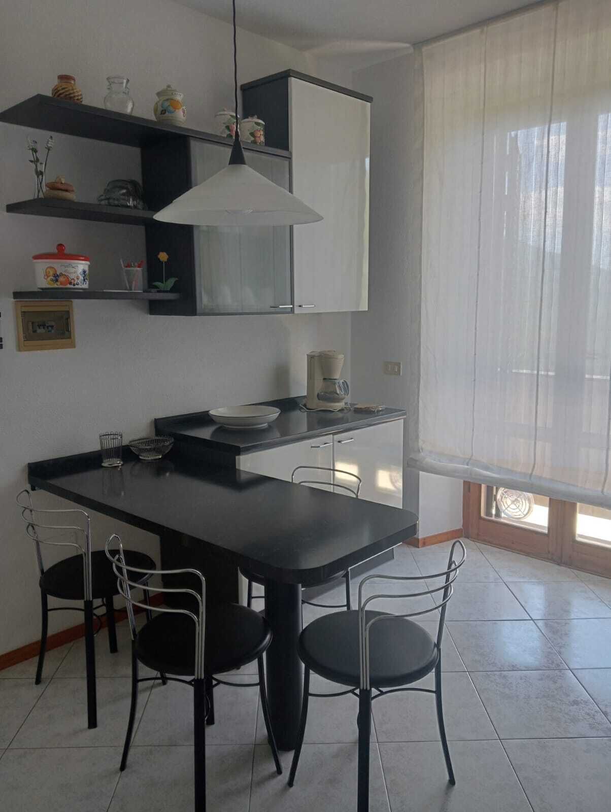 Una cucina moderna con isola centrale, sedie nere e lampada a sospensione.