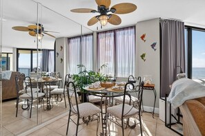 Una habitación de hotel con balcón, zona de comedor con una mesa redonda y sillas, y ventilador de techo.