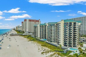 Un hotel frente a la playa con varios edificios de gran altura, una playa arenosa y un cielo azul despejado.