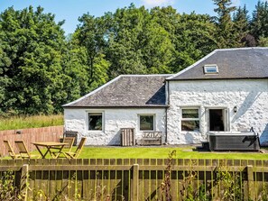 Ein weißes Haus mit geneigtem Dach, einer Holzterrasse und einem Whirlpool im Garten.
