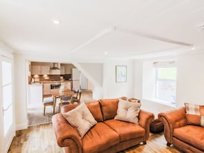 Ein geräumiges Wohnzimmer mit einer großen braunen Ledersofa, einem Essbereich mit Holztisch und -stühlen sowie einer Küche im Hintergrund.