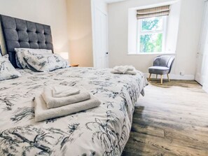Ein Schlafzimmer mit einem großen Bett, einem Sessel, einem Fenster mit Ausblick und einer Tür.