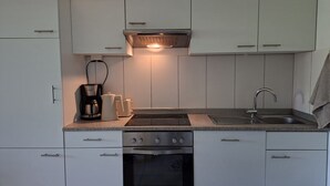 Eine moderne Küche mit weißen Schränken, einem Einbauofen, einem Kochfeld und einer Kaffeemaschine.
