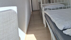 Ein schmaler Flur führt zu einem Schlafzimmer mit Etagenbetten, einem Kleiderschrank und einem Regal mit Dekoration.