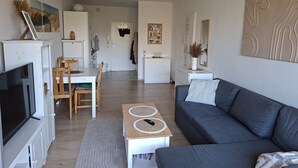 Ein modernes Wohnzimmer mit grauem Sofa, Fernseher und Essbereich mit Tisch und Stühlen.