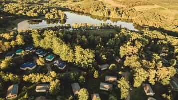 An aerial view of a campground with multiple cabins, a lake, and surrounding forested hills.
