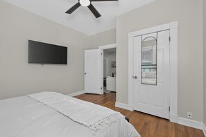A bedroom with a bed, a television, a door, and a ceiling fan.