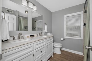 Een badkamer met een wastafelmeubel met dubbele wastafel, een toilet, een douche met glazen deur en een raam met zonwering.