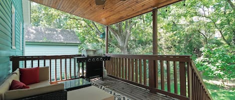 A covered outdoor deck with a ceiling fan, a grill, and a seating area with cushions.
