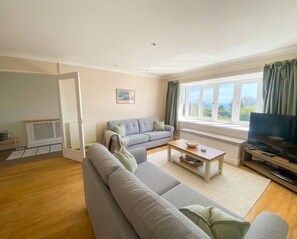 Ein Wohnzimmer mit Sofa, Couchtisch, Fernseher und einem Fenster mit Vorhängen.