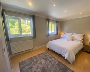 Ein Schlafzimmer mit einem großen Bett, zwei mit Vorhängen versehenen Fenstern, einem Heizkörper und einem grauen Teppich.