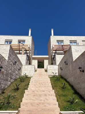 A modern building with a central entrance, stone walls, and a staircase leading up to it. - Becici Hills Adriatic Villas (Bečići)