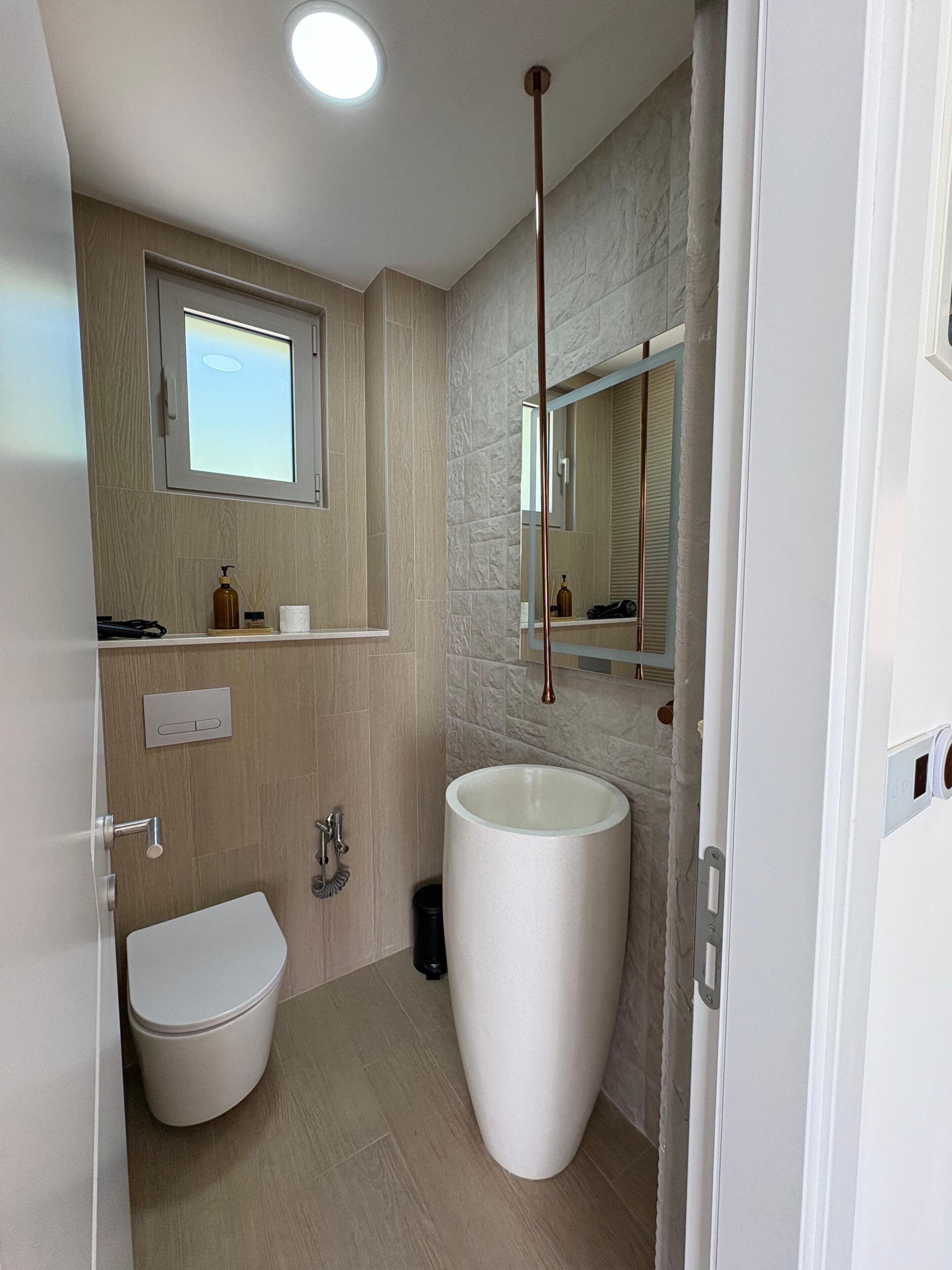 Et moderne badeværelse med toilet, stor vask, spejl og vindue.