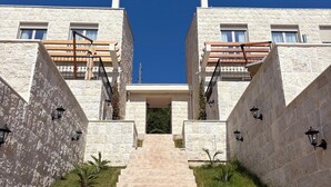 A modern building with a central entrance, stone walls, and a staircase leading up to it. - Becici Hills Adriatic Villas (Bečići)