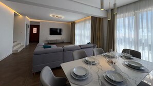 A modern living room with a sofa, dining table set for four, and a TV mounted on the wall. - Becici Hills Adriatic Villas (Bečići)
