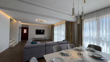 A modern living room with a sofa, dining table set for four, and a TV mounted on the wall.