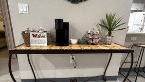 Ein Empfangsbereich mit einer Kaffeestation, einem Willkommensschild, einem an der Wand befestigten Willkommensschild, einer Topfpflanze und einer Kaffeemaschine.