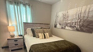 Ein Schlafzimmer mit Bett, Nachttisch, Lampe, Deckenventilator und Wandbild.