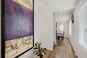 A hallway with a dining area, white walls, and a large abstract painting. - Fully Furnished Retreat Near Tesla Gigafactory and Cotaland Theme Park (Austin)