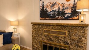 A living room with a stone fireplace, a painting of mountains, a sofa, and a lamp. - Alpine Escape in Ruidoso NM (Ruidoso)