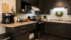 A modern kitchen with dark cabinetry, a microwave, stove, and a coffee maker. - Alpine Escape in Ruidoso NM (Ruidoso)