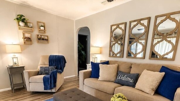 A living room with a sofa, ottoman, side table, lamps, decorative mirrors, and a blue carpet. - Alpine Escape in Ruidoso NM (Ruidoso)