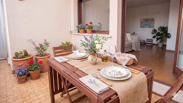 An outdoor dining area with a wooden table set for two, surrounded by potted plants, and a view of the interior through an open door. - Casa Macor (Venice)